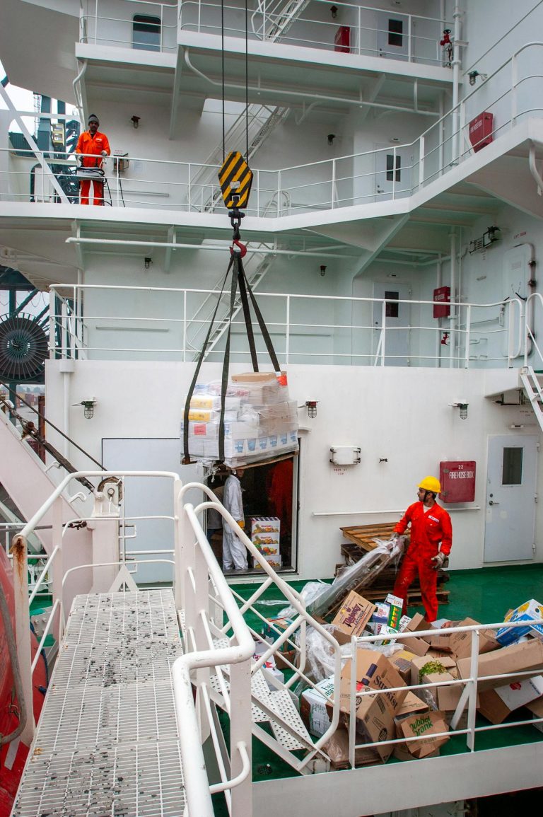 Cargo and maritime workers handling supply transfer on a ship deck.