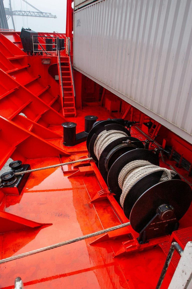 Close-up of a vibrant red ship deck featuring mooring equipment and marine ropes.